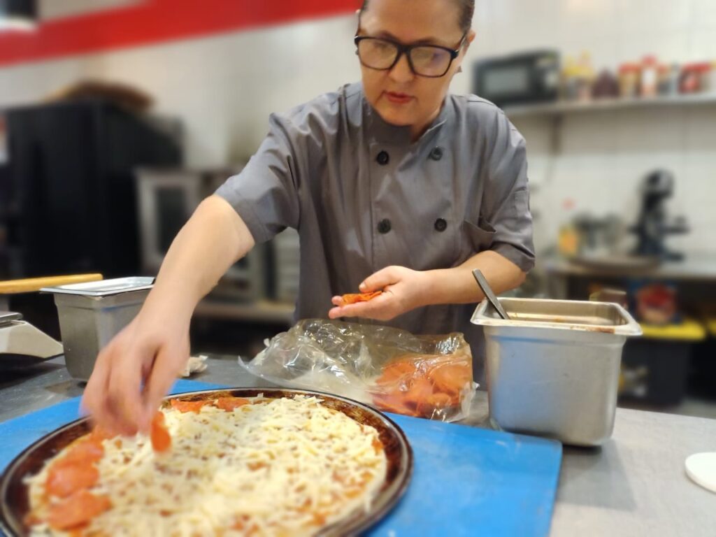 Marcela working in the school restaurant making a pizza